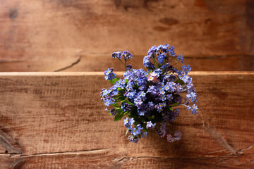 Fototapeta premium Blue wildflowers in a glass cup on a wooden background. Forget me nots.