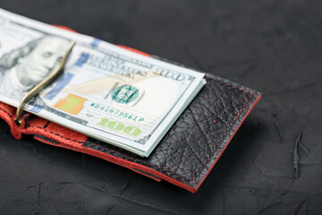 Red purse with new dollars on a black background.