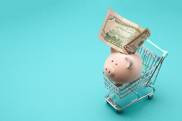 Toy pink piggy bank inside shopping cart isolated on aquamarine background 