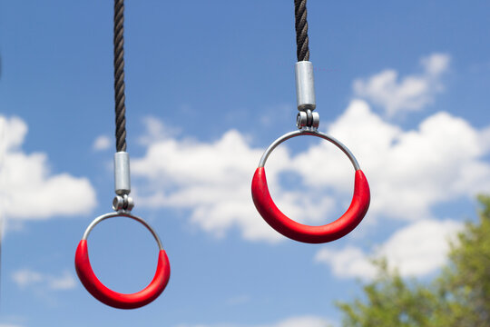 Gymnastic rings hanging in sunlight.  cloudy sky in the background