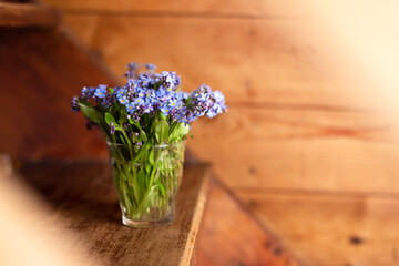 Blue wildflowers in a glass cup on a wooden background. Forget me nots.