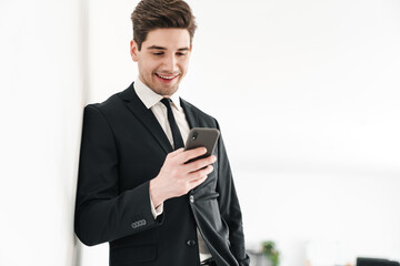 Naklejka premium Image of smiling businessman wearing black suit using mobile phone
