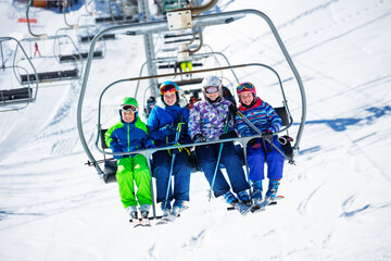 Group of skiers children sit on chairlift going on the mountain to ski, sitting together smiling