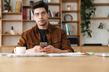 Fototapeta na wymiar Image of handsome young man using mobile phone while working