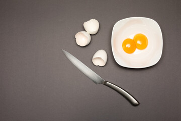 Cracked egg and knifeon gray background
