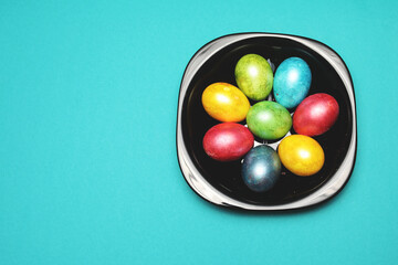 many colors eggs on black plate isolated on aquamarine background