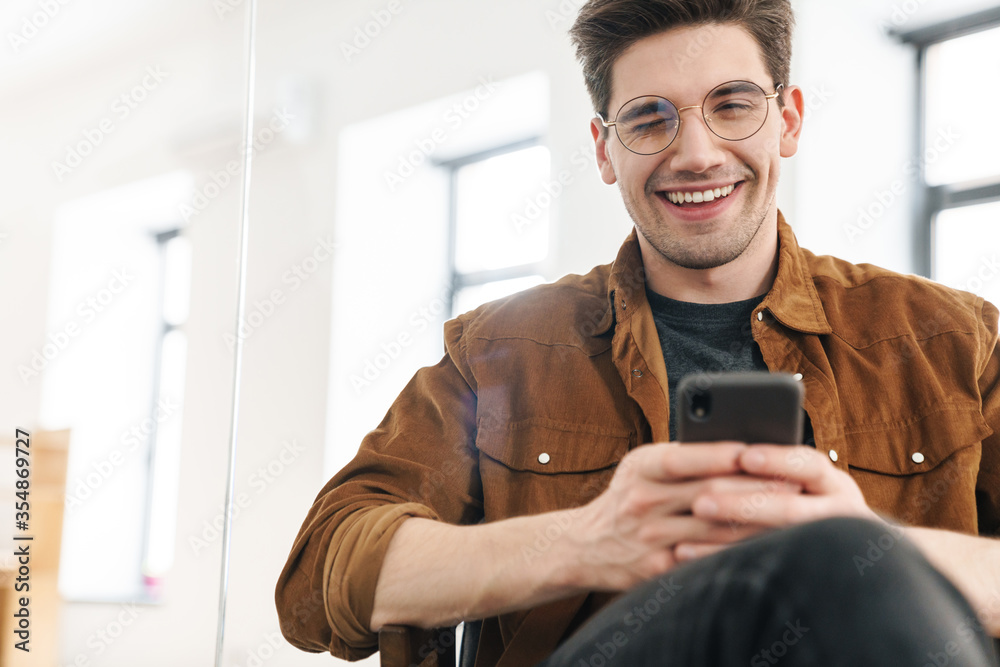 Sticker Image of joyful young man winking and using cellphone while working