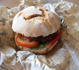 Homemade freshly prepared burger with grilled beef patty, tomato, lettuce and bun on a paper. Simple and delicious food