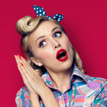 Excited surprised beauty woman. Girl in pin up fashion style, holding hands palm to palm near face. Retro and vintage concept. Red color background.