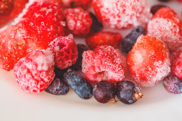 Different frozen berries on a white plate. Raspberries, strawberries and black currants.