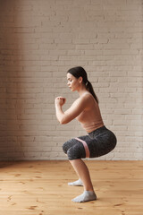 Young woman making squats with rubber resistance band