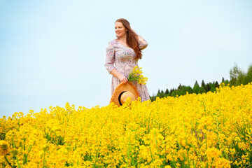Fototapeta premium A red-haired woman in a blooming yellow field walks in flowers. Happiness, joy, youth, outdoor activities.