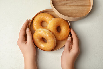 Woman with box of delicious donuts at white table, top view