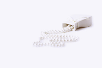 Selective focus of a string of white pearls spilled from an old overturned white vase. Isolated white background, copy space.