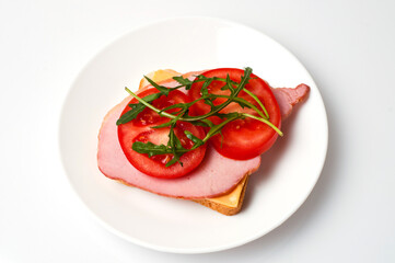 Sandwich of balyk, cheese, bread, tomatoes and arugula on a white plate on a plate flat lay