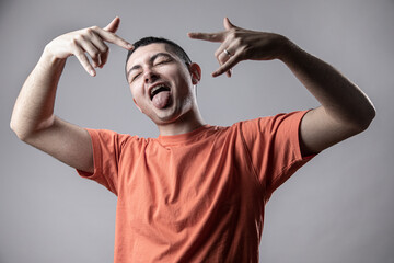 Ragazzo giovane con t-shirt arancione balla divertito facendo le corna con le mani stile rapper,...