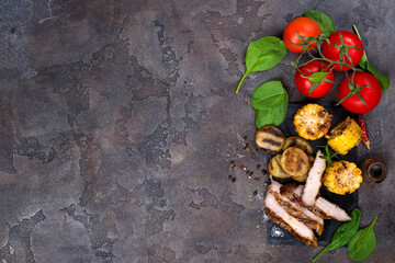 sliced pork steak and grilled vegetables on slate board on stone table.