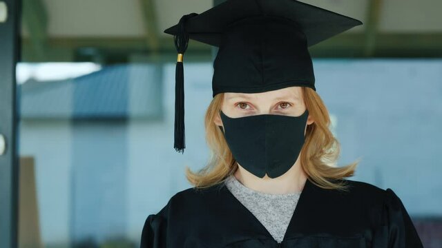 Portrait of a masked graduate on the doorstep of the university