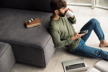 Image of man drinking coffee and using mobile phone while sitting