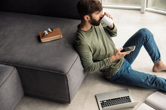 Image of man drinking coffee and using mobile phone while sitting