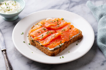 Sandwich, toast with smoked salmon and cream cheese on white plate. Marble background. Close up.