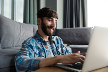 Image of laughing man working with notebook while sitting on floor