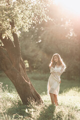 Portrait of a beautiful young blond woman in a white dress in a boho style walks in the park in...