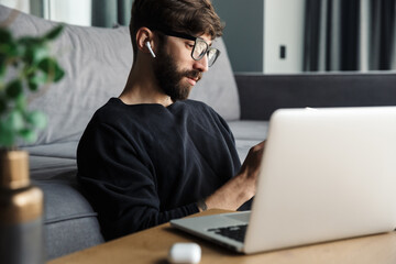 Image of man using notebook and wireless earphones while sitting