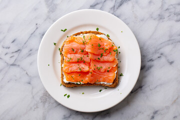Sandwich, toast with smoked salmon and cream cheese on white plate. Marble background. Top view.