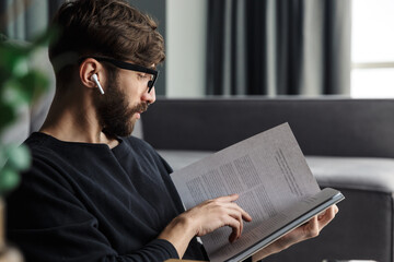 Image of focused man drinking coffee and reading magazine while sitting