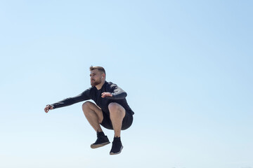 Fototapeta na wymiar Portrait of a young bearded athlete of twenty-five, jumping against a blue sky.