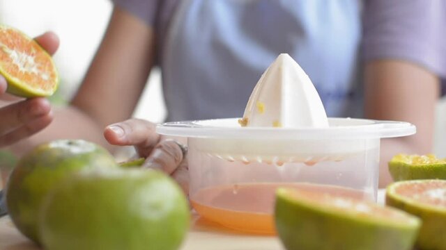 Close up hands of housewife is cutting and squeezing orange juice with squeezer while preparing breakfast at home. Homemade. Healthy lifestyle. Slow motion.