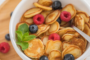 Bowl for breakfast with tiny pancake cereal with blueberries, raspberries, mint