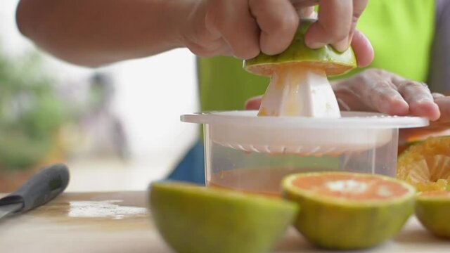 Close up hands of housewife is squeezing orange juice with squeezer while preparing breakfast at home. Homemade. Healthy lifestyle. Slow motion.