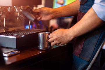 Barista steaming milk in the pitcher with coffee machine for  preparing to make latte art.
