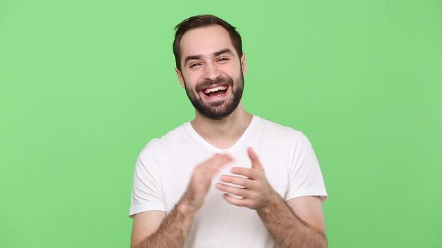 Happy bearded young guy 20s in white t-shirt isolated on green chroma key background studio. People sincere emotion lifestyle concept. Looking at camera charming smile applause cheering clapping hands