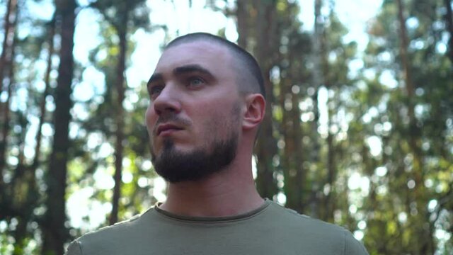 Portrait of a Serious Young Man Who Looks Around and Strokes Beard. Short-haired man. In the Background Blurred Forest.