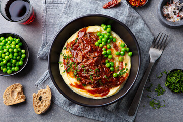 Mashed potatoes with beef meat and green peas in bowl. Grey background. Copy space. Top view.
