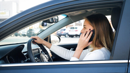 Portrait of young businesswoman using smartphone while driving a car. Driver may be distrated that may cause car accident
