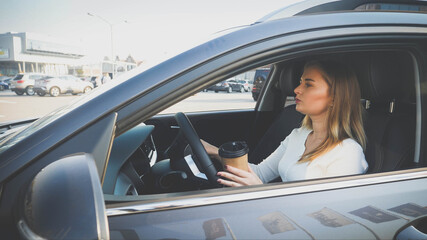 Toned portrait of female driver with coffee in paper cup commuting to work at morning