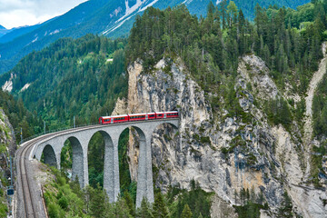 Red train passes above the Landwasser Viaduct bridge, in canton of Graubünden, Switzerland. Bernina Express / Glacier Express uses this railroad.