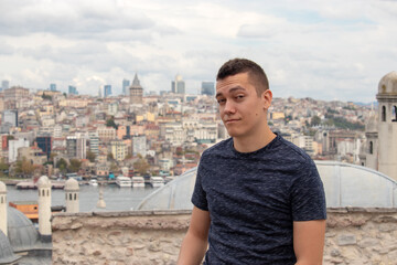 Attractive young adult man making a funny face posing in istanbul white travelling, view of the city seen blurred behing in the distance. Galata tower peeking above all other buildings