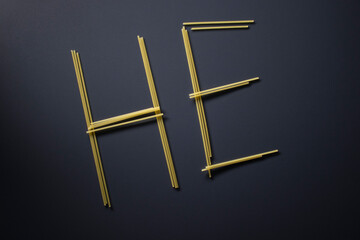 Word 'HE' written with spaghetti on gray background, top view, copy space. Food supplies, food donation on quarantine while coronavirus.