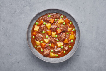 Irish Beef Stew in matt gray bowl on concrete background. Stew with beef or lamb meat with potatoes, carrots, peas and herbs. Traditional american and european food. Dinner mear