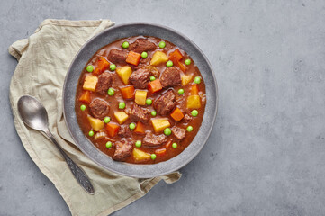 Irish Beef Stew in matt gray bowl on concrete background. Stew with beef or lamb meat with potatoes, carrots, peas and herbs. Traditional american and european food. Dinner meal. Copy space