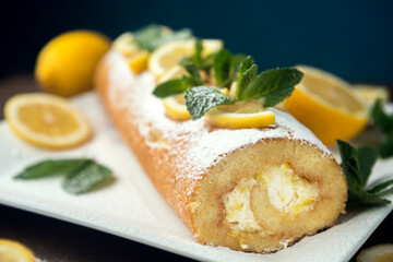 Lemon roll cake decorated with slices of lemon fruit and leaves of mint