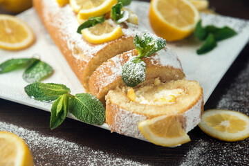 Lemon roll cake decorated with slices of lemon fruit and leaves of mint