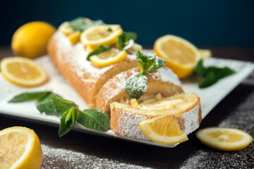 Lemon roll cake decorated with slices of lemon fruit and leaves of mint