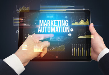 Close-up of hands holding tablet with MARKETING AUTOMATION inscription, modern business concept