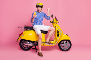 Fototapeta na wymiar Portrait of his he nice attractive handsome cheerful cheery glad ecstatic guy sitting on moped using cell app 5g celebrating like reaction isolated over pink pastel color background